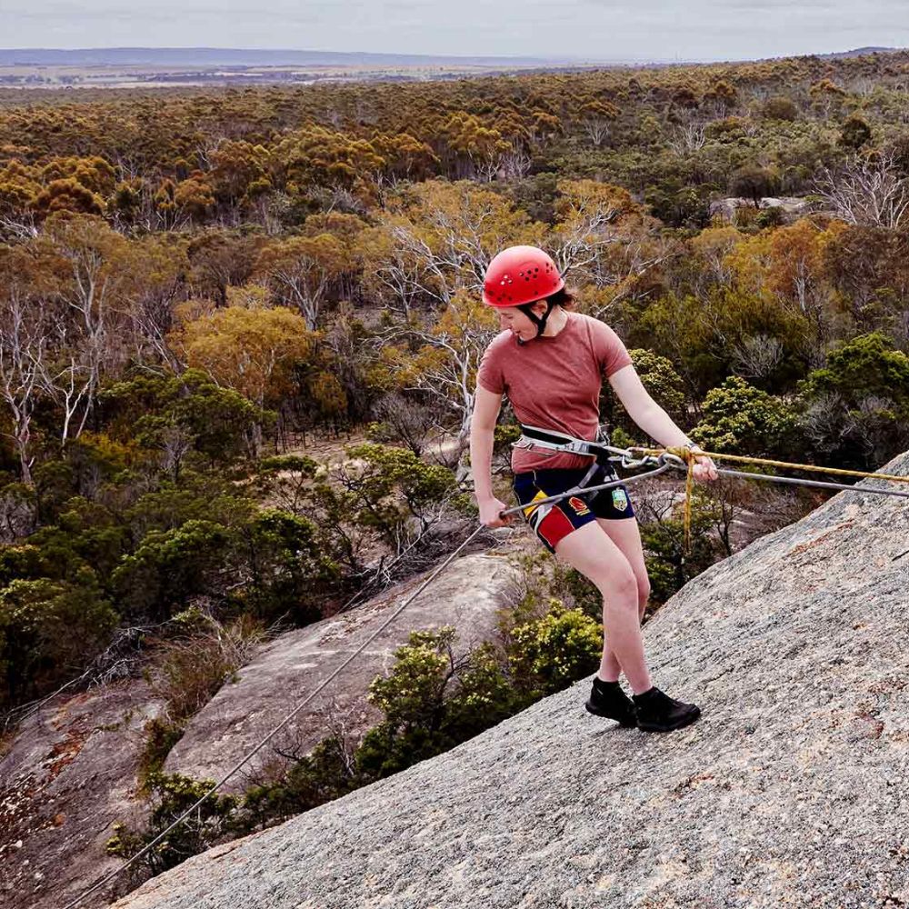 Person on a rock face with safety equipment in a forested area